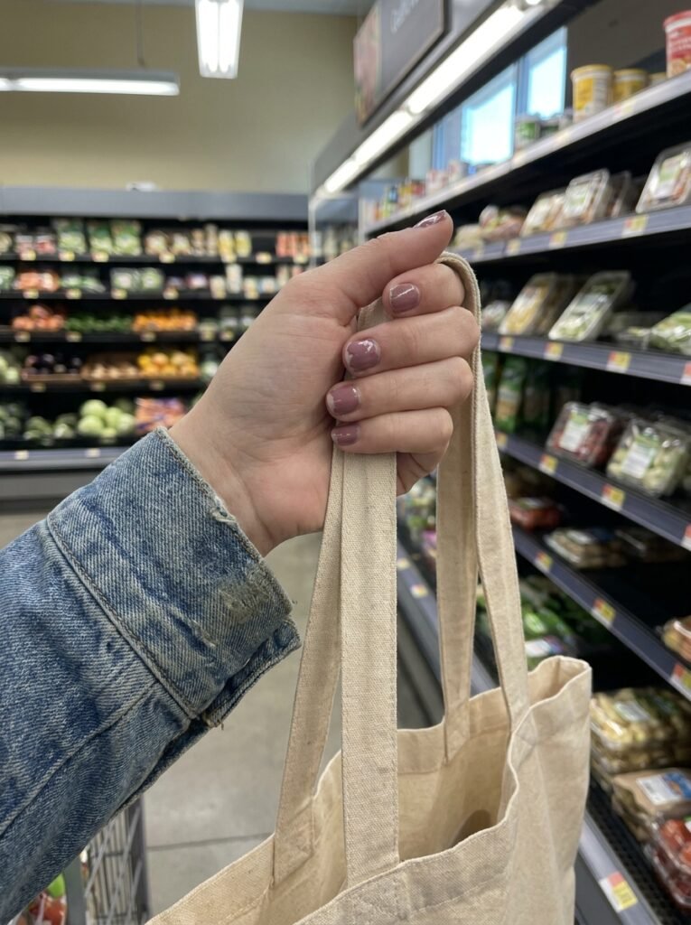 Slightly worn mauve manicure on hands holding a shopping bag in a supermarket.