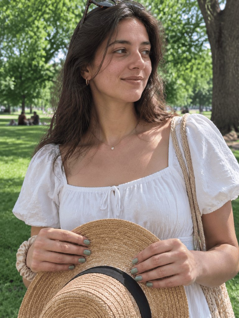 Sage green nails holding a straw hat outdoors on a sunny day
