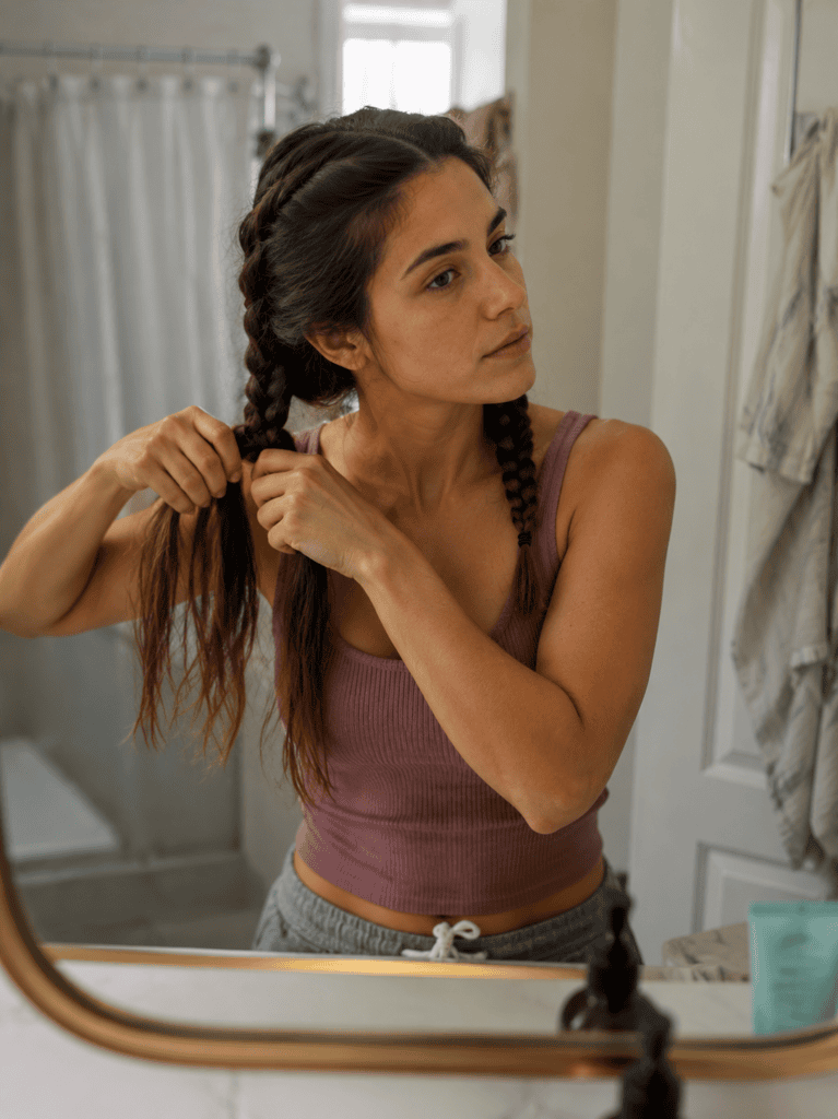 Woman braiding double Dutch braids in her long brown hair at a mirror