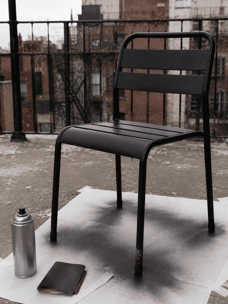 Flea market metal chair drying after a matte black spray paint makeover on a city rooftop