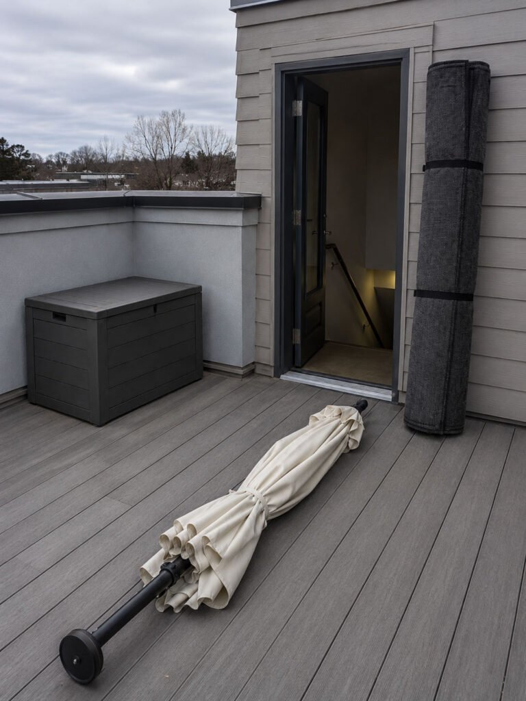 A closed umbrella laid flat and a rolled rug standing by a rooftop doorway under a grey sky