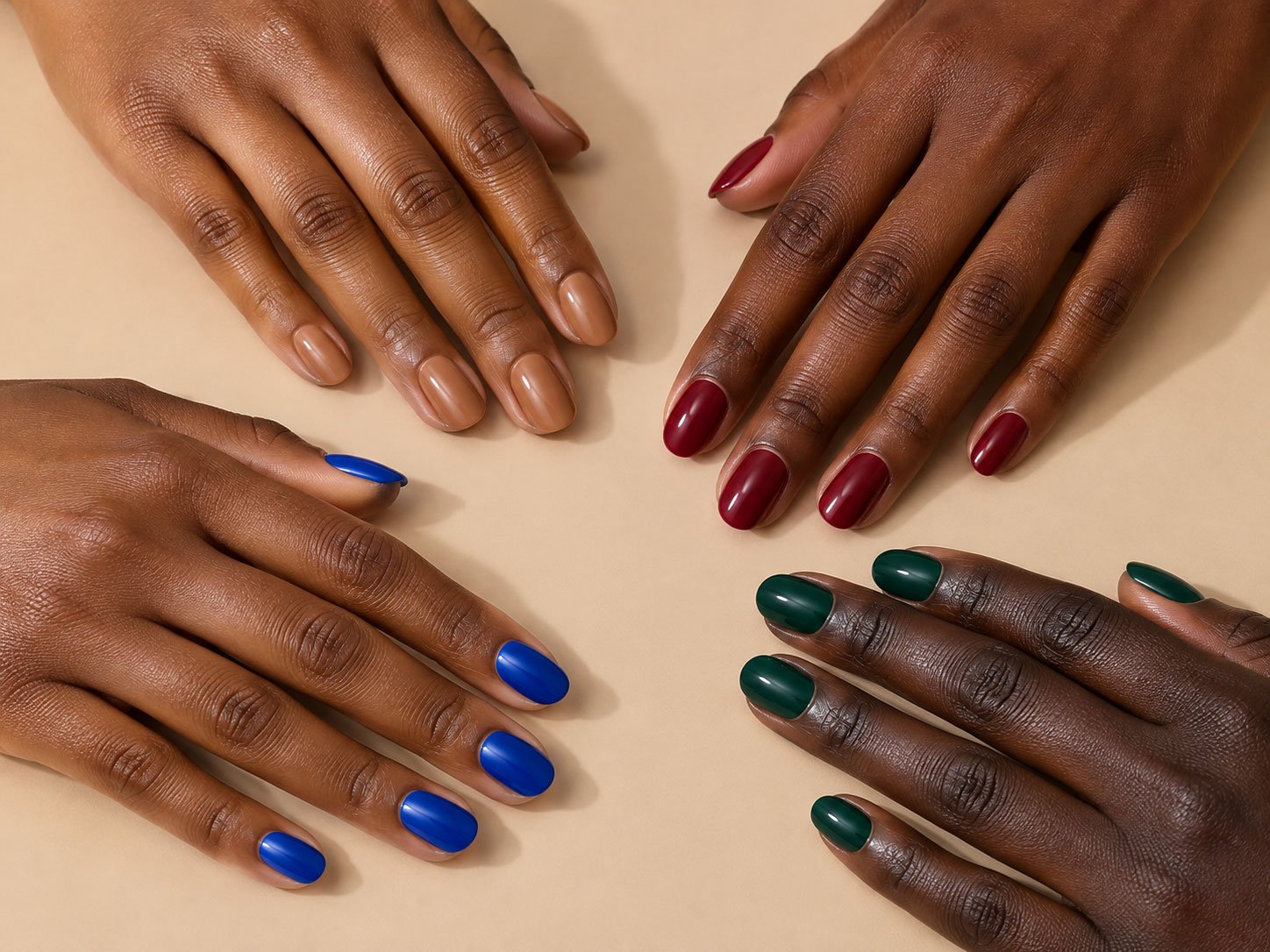 Four hands with medium deep to very deep brown skin wearing nude, burgundy, cobalt blue and emerald green manicures.